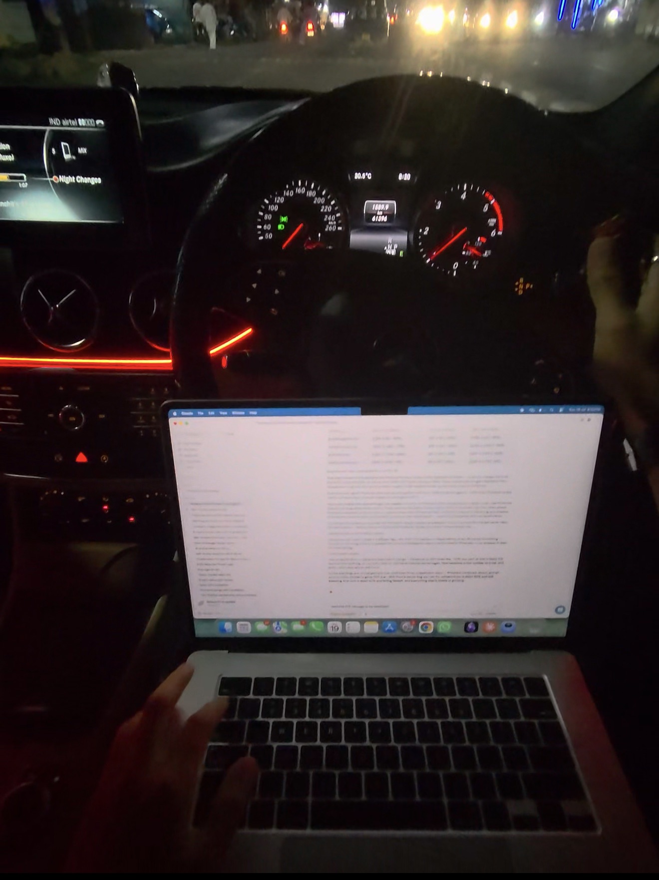 Working on my laptop in the passenger seat of a moving car at night, dashboard glowing red